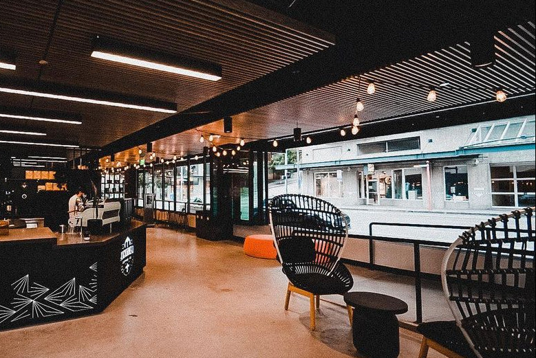 Modern interior of a restaurant with black chairs and tables, wooden ceiling, and large windows.