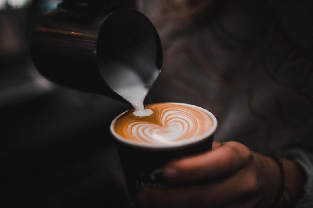 Person pouring steamed milk into a cup of coffee with latte art.
