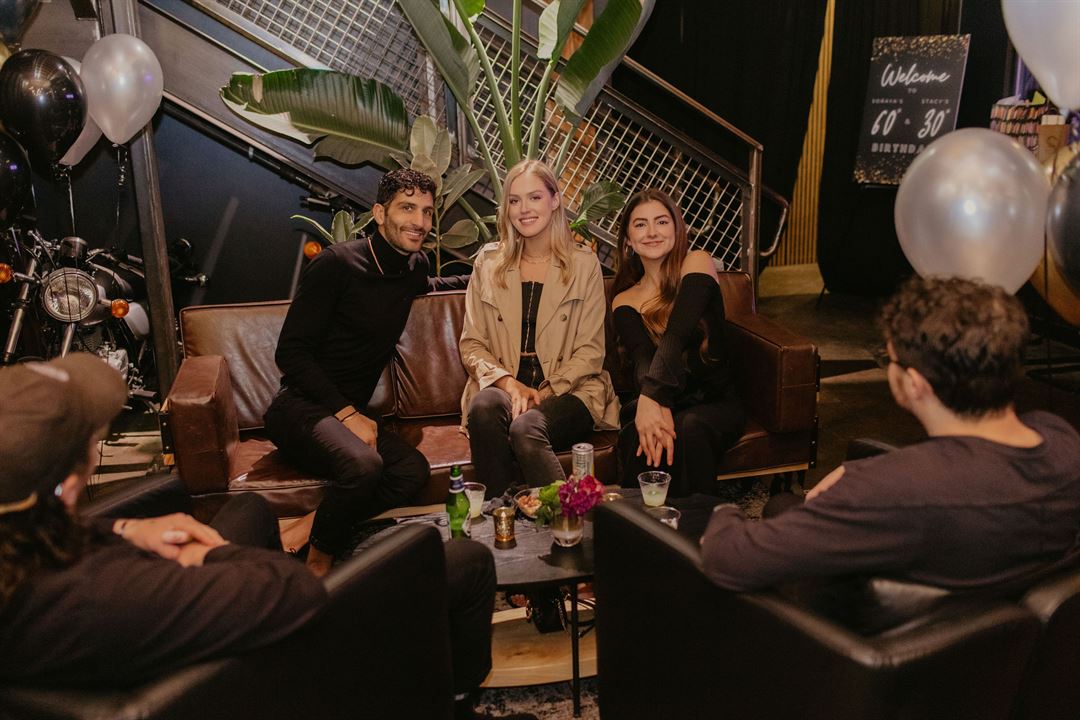 Group of people sitting in a stylish room with balloons and a motorcycle in the background