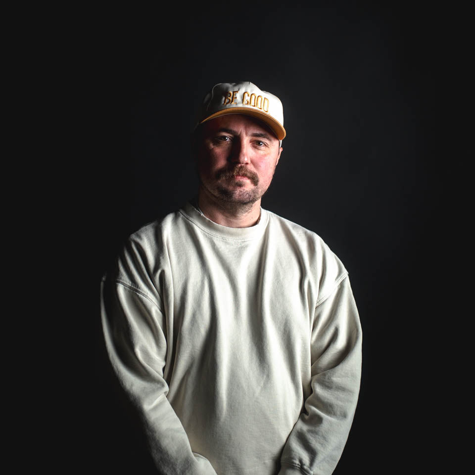 Man wearing a white cap and long-sleeve shirt against a black background