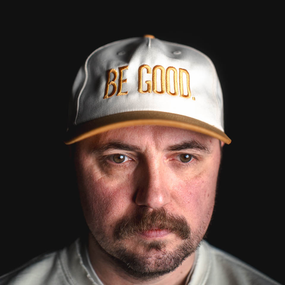 Man wearing a cap with 'BE GOOD' text on a black background