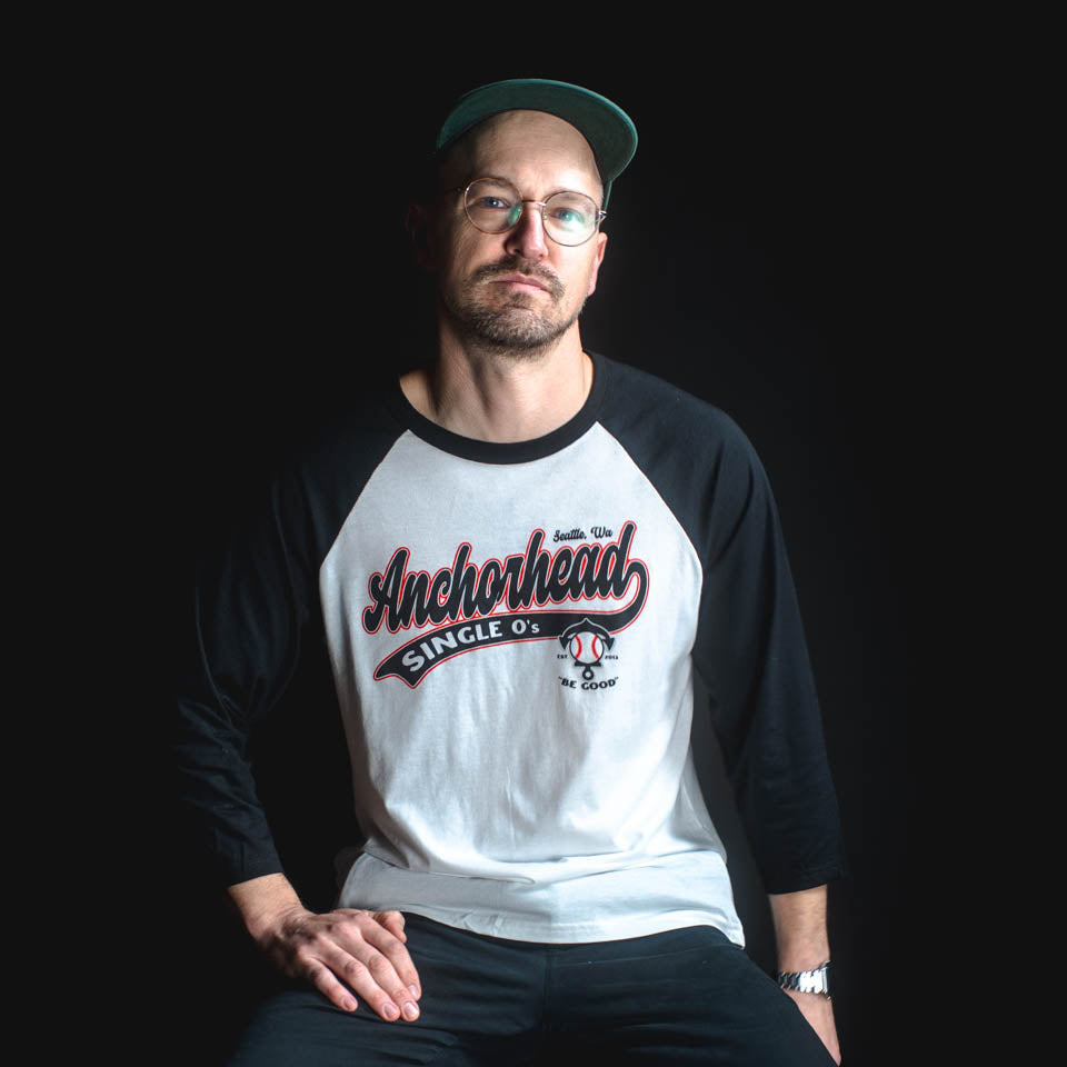 Man wearing a black and white 'Anchorhead' baseball shirt against a black background