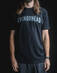 Person wearing a black t-shirt with 'ANCHORHEAD' printed on it against a dark background