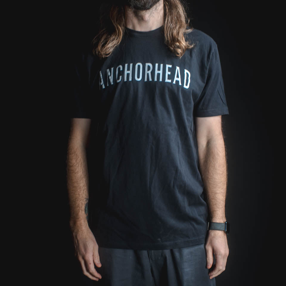 Person wearing a black t-shirt with 'ANCHORHEAD' printed on it against a dark background