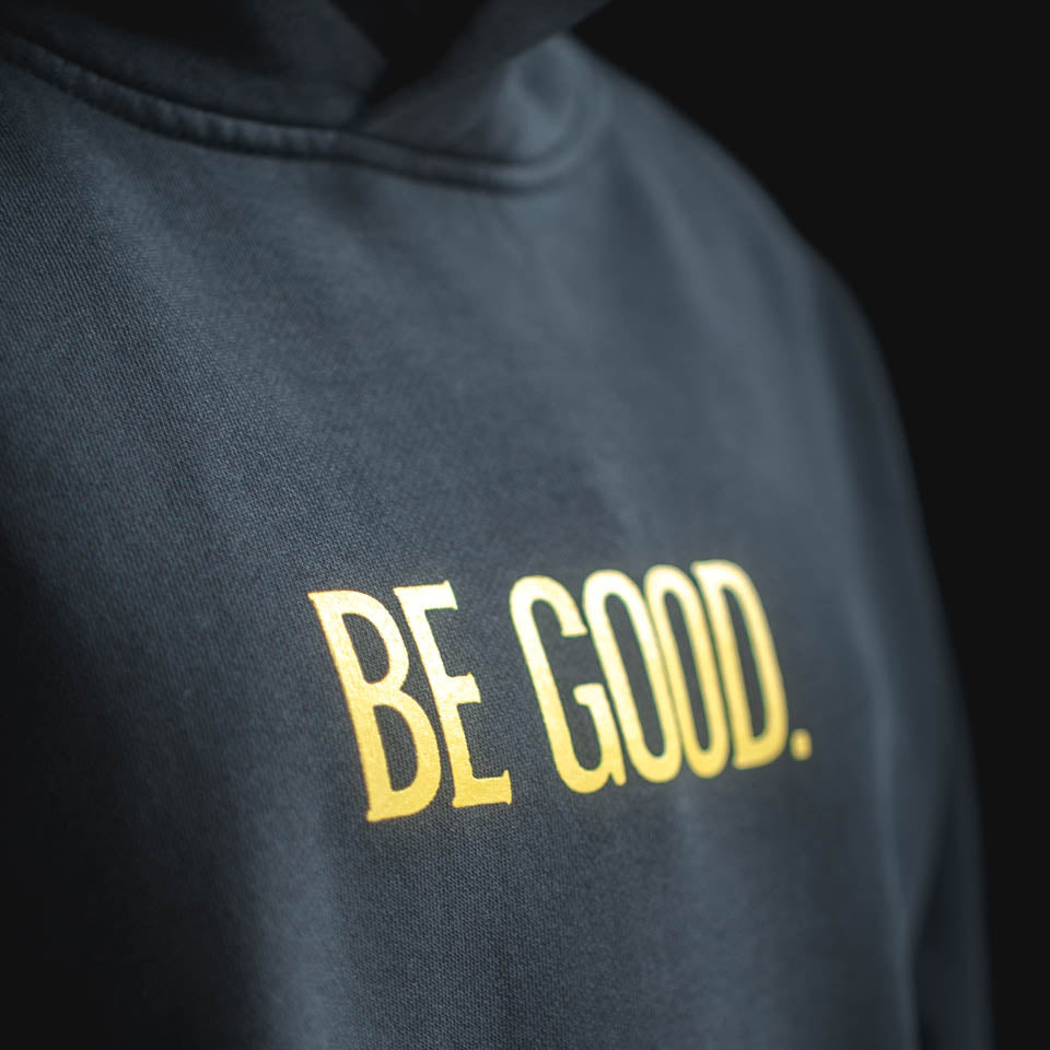 Black hoodie with 'BE GOOD.' text in gold on a black background