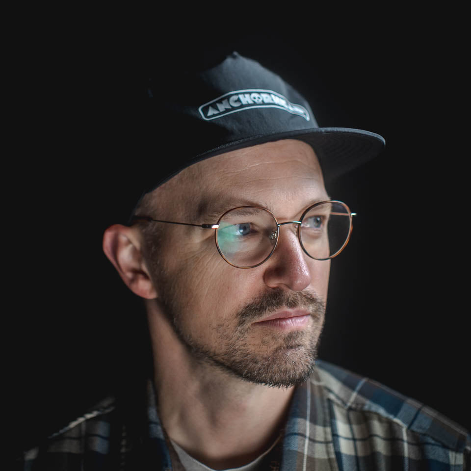 Man wearing a black cap and round glasses against a dark background