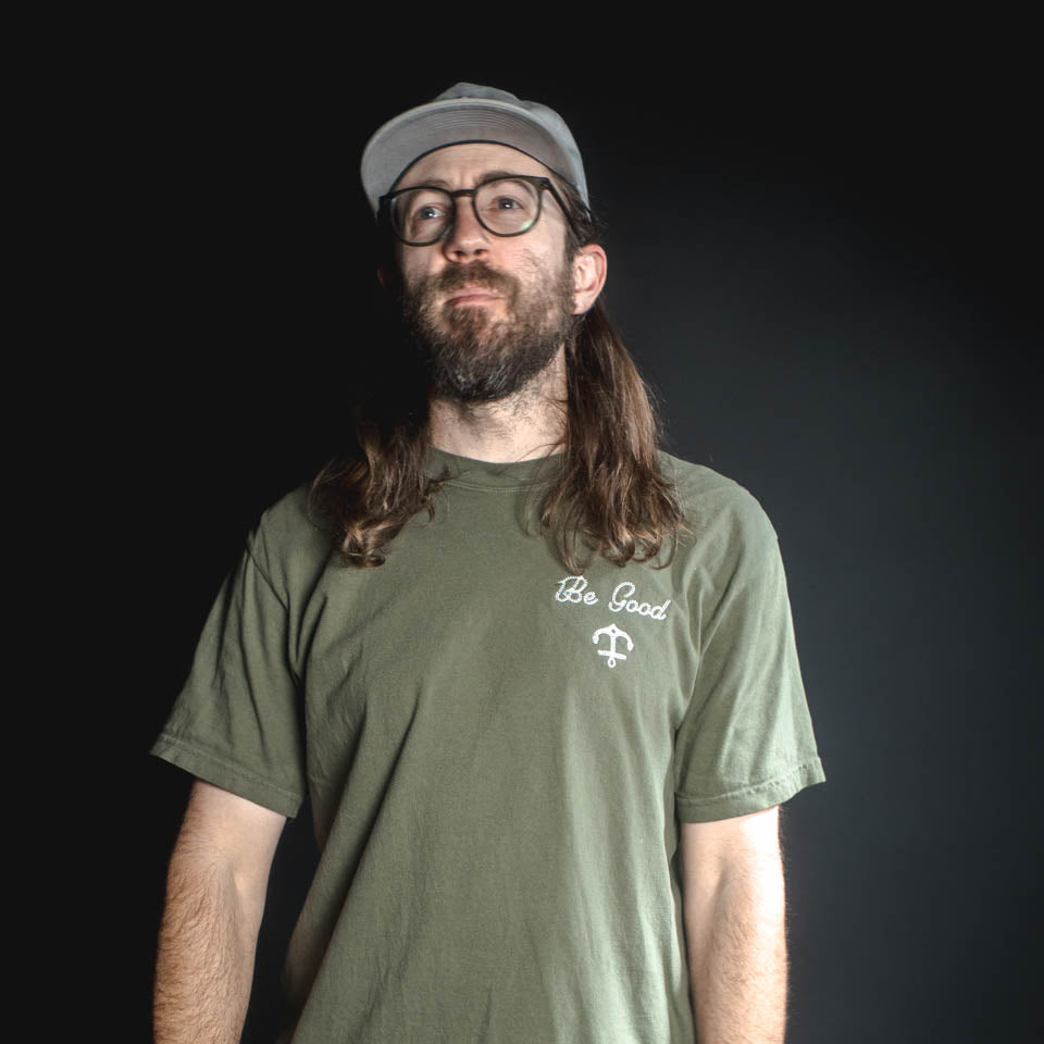 Man wearing a green t-shirt with 'Be Good' text on a dark background