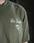Green t-shirt with 'Be Good' text and symbol on a dark background