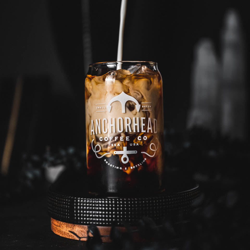 A dark-colored glass can with 'Anchorhead Coffee Co' printed on it, filled with a beverage, presented on a dark background.